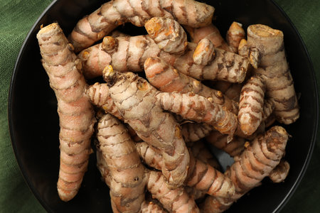 Bowl with raw turmeric roots on table, top view