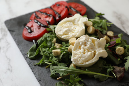 Delicious burrata cheese, tomatoes and arugula on white marble table, closeup