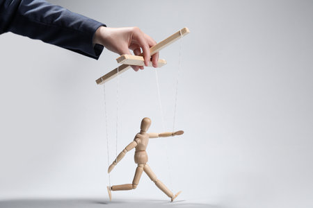 Woman pulling strings of puppet on light gray background, closeup. Space for text