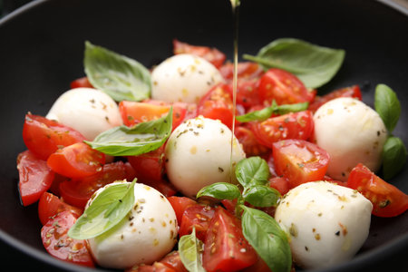 Pouring butter onto tasty salad Caprese with tomatoes, mozzarella balls and basil, closeup