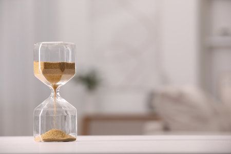 Hourglass with flowing sand on white table against blurred background. Space for textの写真素材