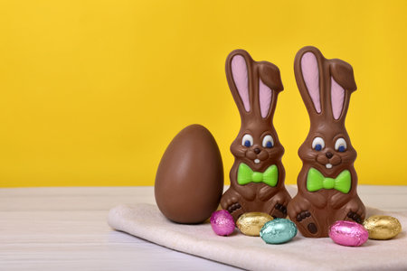 Chocolate Easter bunnies and eggs on white wooden table against yellow background. Space for textの写真素材