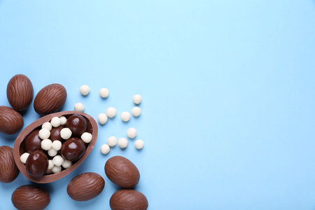 Delicious chocolate eggs and candies on light blue background, flat lay. Space for textの写真素材