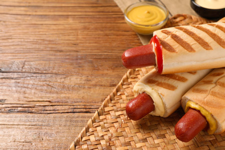 Tasty French hot dogs with different sauces on wooden table, closeup. Space for textの写真素材