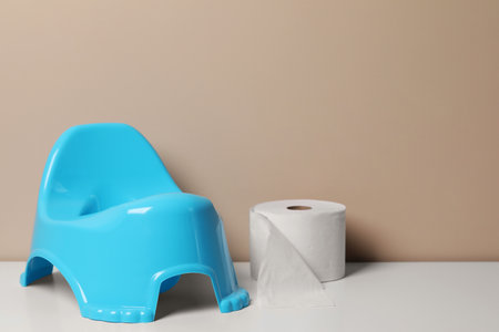 Light blue baby potty and toilet paper on white table near brown wall, space for textの写真素材