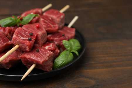 Skewers with cut fresh beef meat, basil leaves and spices on wooden table, closeup. Space for textの写真素材