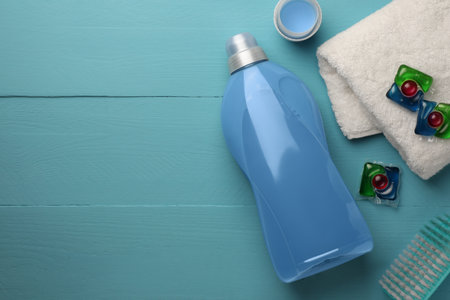 Bottle of fabric softener, laundry capsules and towel on light blue wooden table, flat lay. Space for textの写真素材