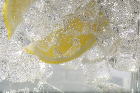 Juicy lemon slices and ice cubes in soda water against white background, closeupの写真素材