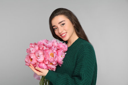Beautiful young woman with bouquet of peonies on light gray backgroundの写真素材