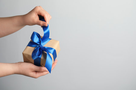 Woman holding gift box with blue bow on light gray background, closeup. Space for textの写真素材