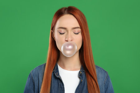 Beautiful woman blowing bubble gum on green backgroundの写真素材