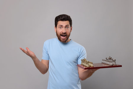 Emotional man holding chessboard with game pieces on light gray backgroundの写真素材