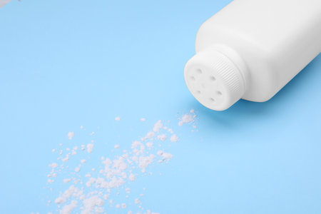 Bottle and scattered dusting powder on light blue background. Baby cosmetic productの写真素材