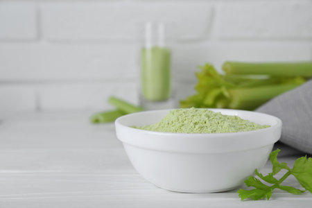 Natural celery powder in bowl and fresh stalks on white table, closeup. Space for textの写真素材
