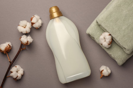 Bottle of fabric softener, terry towels and beautiful cotton flowers on gray background, flat layの写真素材