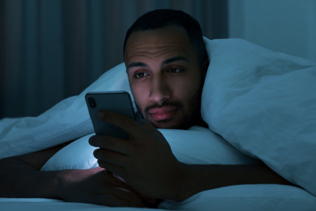 Young man using smartphone under blanket in bed at night. Internet addictionの写真素材