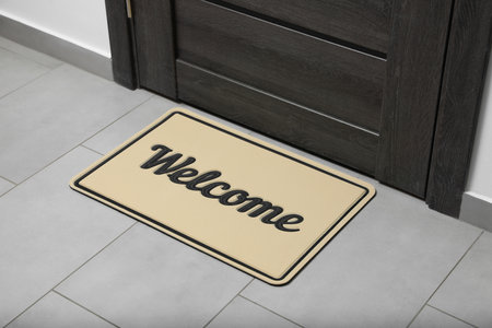 Beautiful beige doormat with the word Welcome on floor near entranceの写真素材