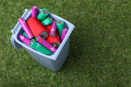 Many used batteries in recycling bin on green grass, above view. Space for textの写真素材