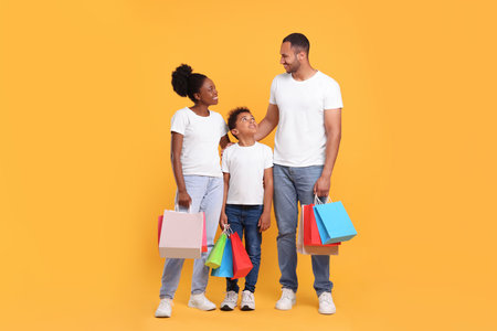 Family shopping. Happy parents and son with colorful bags on orange backgroundの写真素材