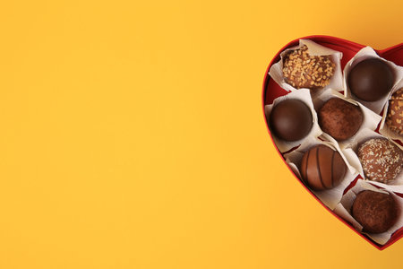 Heart shaped box with delicious chocolate candies on yellow background, top view. Space for textの写真素材