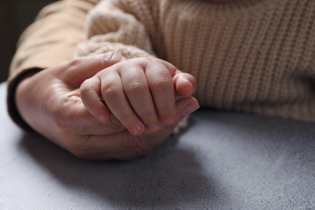 Woman holding hands with her little daughter at light gray table, closeupの写真素材
