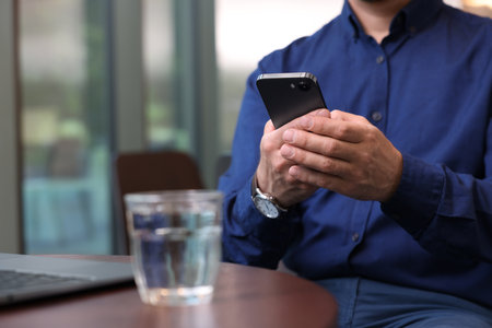 Man sending message via smartphone at table indoors, closeupの写真素材