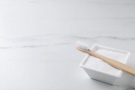 Bamboo toothbrush and bowl of baking soda on white table, closeup. Space for textの写真素材