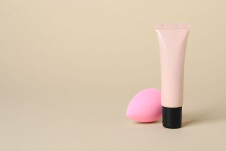 Tube of skin foundation and sponge on beige background, space for text. Makeup productの写真素材