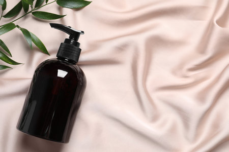 Bottle of cosmetic product and leaves on pink fabric, flat lay. Space for textの写真素材
