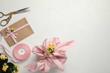 Furoshiki technique. Gift packed in pink fabric, card, flowers and scissors on white table, flat lay. Space for textの写真素材