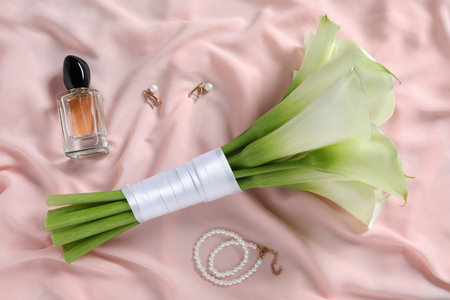 Beautiful calla lily flowers tied with ribbon, bottle of perfume and jewelry on pink fabric, flat layの写真素材