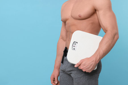 Athletic man holding scales on light blue background, closeup and space for text. Weight loss conceptの写真素材