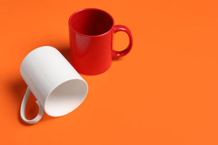 Red and white ceramic mugs on orange background, space for textの写真素材