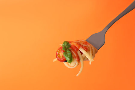 Tasty pasta with tomato sauce and basil on fork against orange background, space for textの写真素材