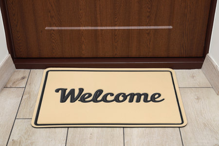 Beautiful beige doormat with the word Welcome on floor near entranceの写真素材