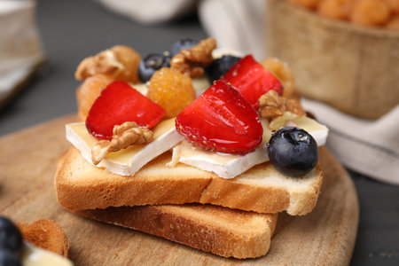 Tasty sandwich with brie cheese, fresh berries and walnuts on gray table, closeup
