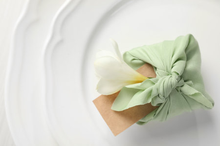 Furoshiki technique. Gift packed in green fabric with flower and blank card on plate, top viewの写真素材