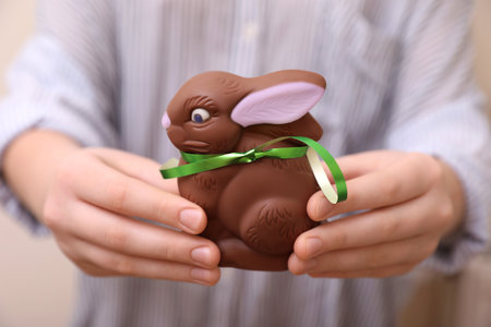 Woman with chocolate Easter bunny on beige background, closeup