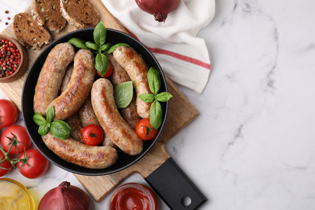 Flat lay composition with tasty homemade sausages, basil leaves and tomatoes in bowl on white marble table. Space for textの写真素材