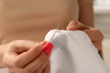 Woman sewing on white fabric with thimble and needle, closeup