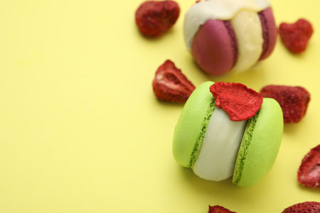 Delicious macarons and dry strawberries on yellow background, closeup. Space for textの写真素材