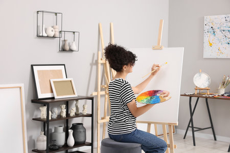 Young woman painting on easel with canvas in studioの写真素材
