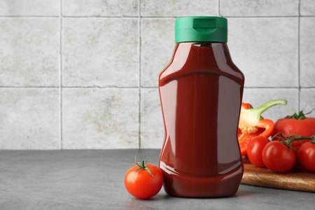 Bottle of tasty ketchup, tomatoes and pepper on gray table. Space for textの写真素材