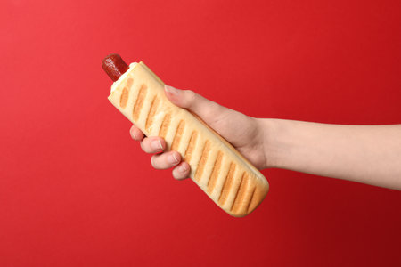 Woman holding delicious French hot dog on red background, closeupの写真素材