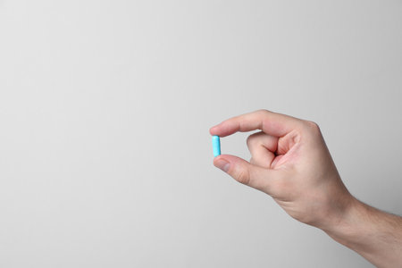 Man holding pill on light gray background, closeup. Space for textの写真素材