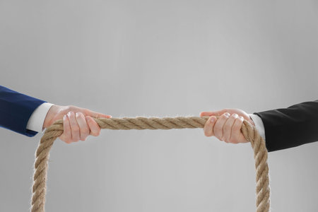 Dispute concept. Men pulling rope on light gray background, closeup