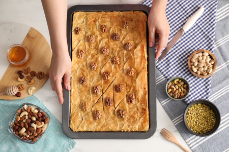 Woman with baking pan of delicious baklava at white table, top view