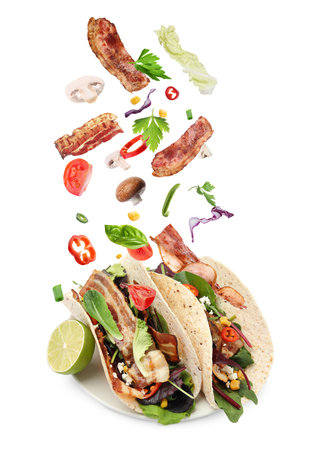 Delicious tacos. Ingredients falling into tortillas on white backgroundの写真素材