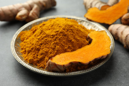 Plate with turmeric powder and cut root on gray table, closeupの写真素材