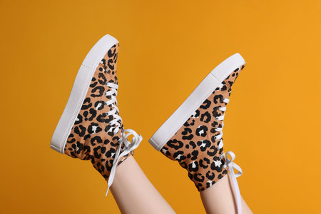 Woman posing in classic old school sneakers with leopard print on orange background, closeup